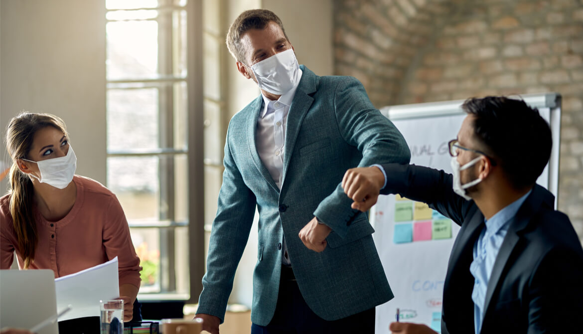 description businessmen do an elbow bump in masks at meeting with another businesswoman
