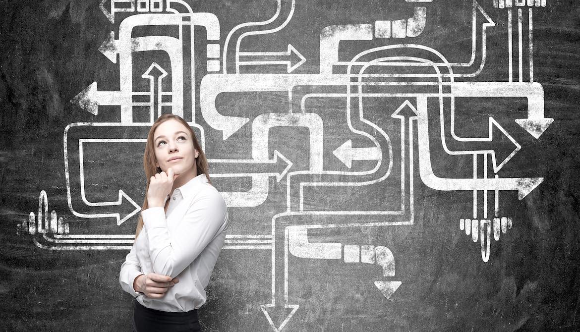 young female leader thinking strategically in front of chalkboard with drawings of many bending arrows