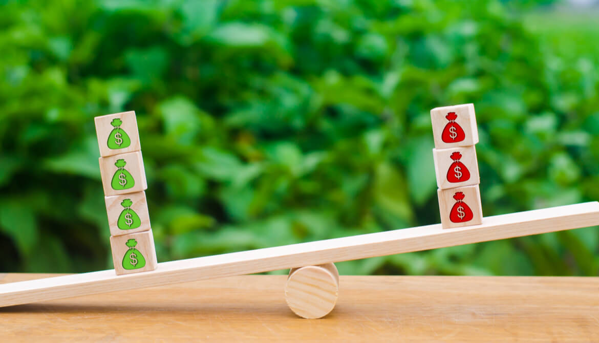 seesaw with balance tipped toward stack of sacks with green dollar signs