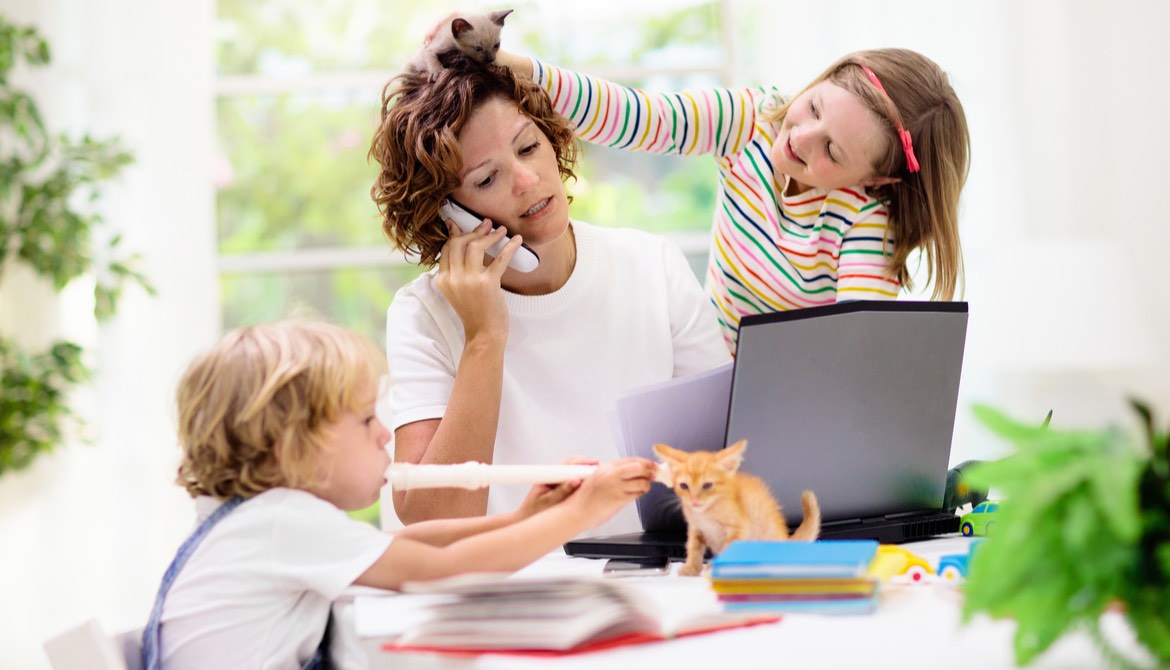 mother working from home on laptop and phone with two young children and kittens playing around her