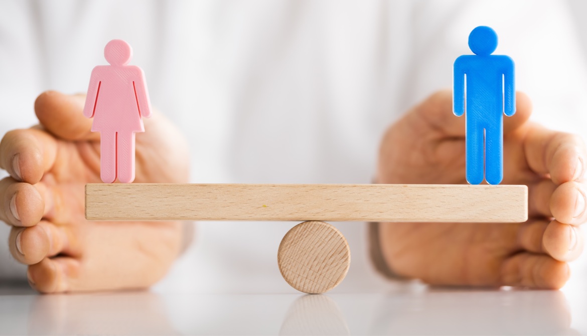 hands balancing pink and blue people figures on equal gender seesaw