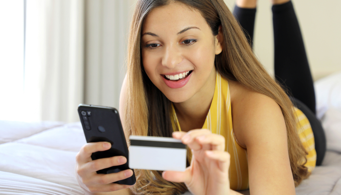 woman laying on a bed using credit card and smart phone