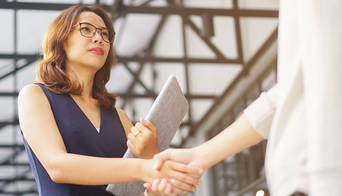 serious looking Asian businesswoman holding a portfolio shakes hands with vendor