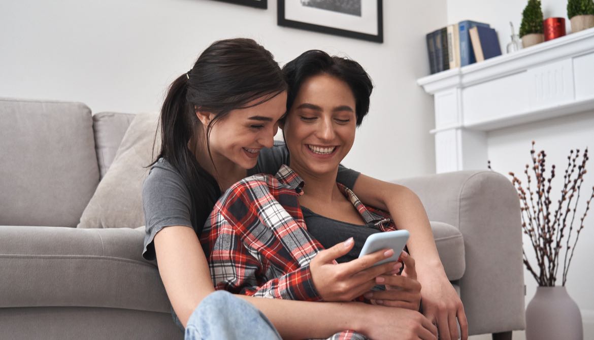 lesbian couple sitting in front of couch using smartphone