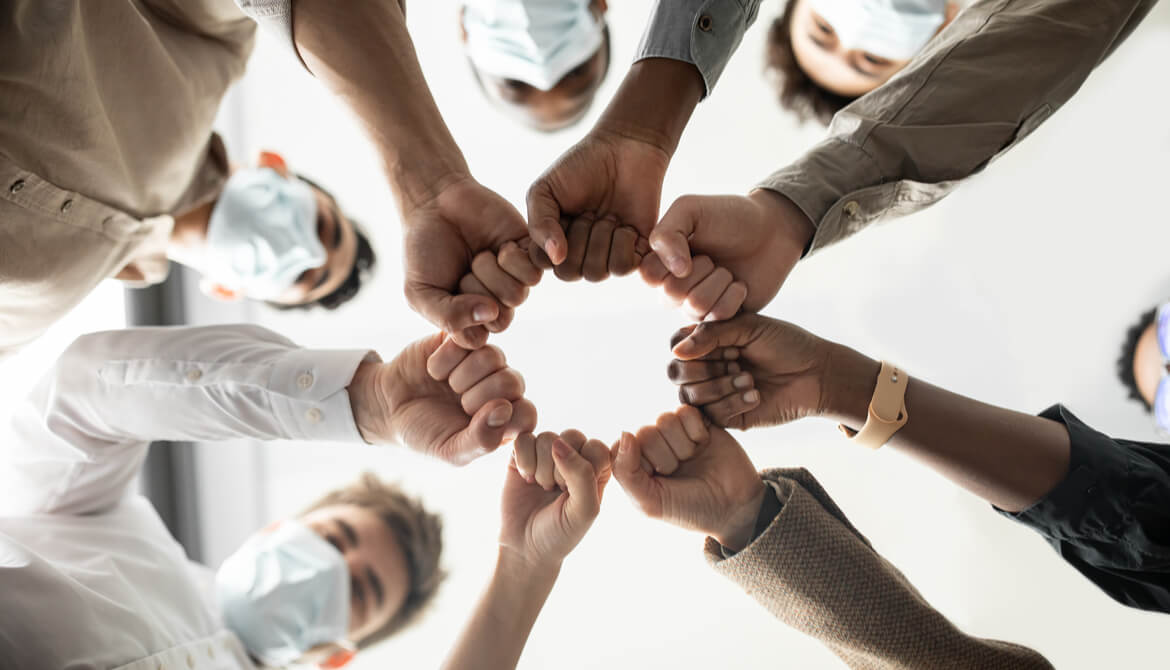 engaged group of masked employees bumping fists in a circle