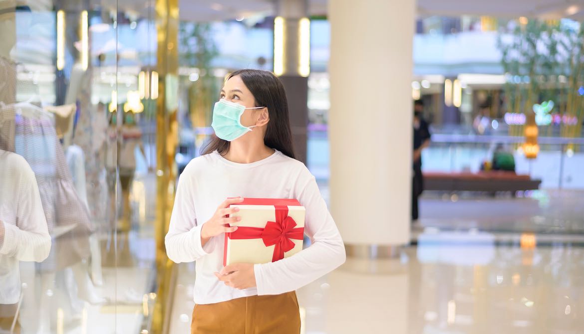 masked woman shopping in mall carrying present with red bow