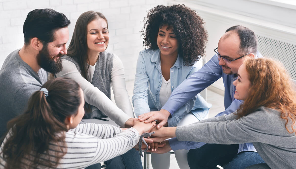 smiling circle of employee team members put hands together to support each other
