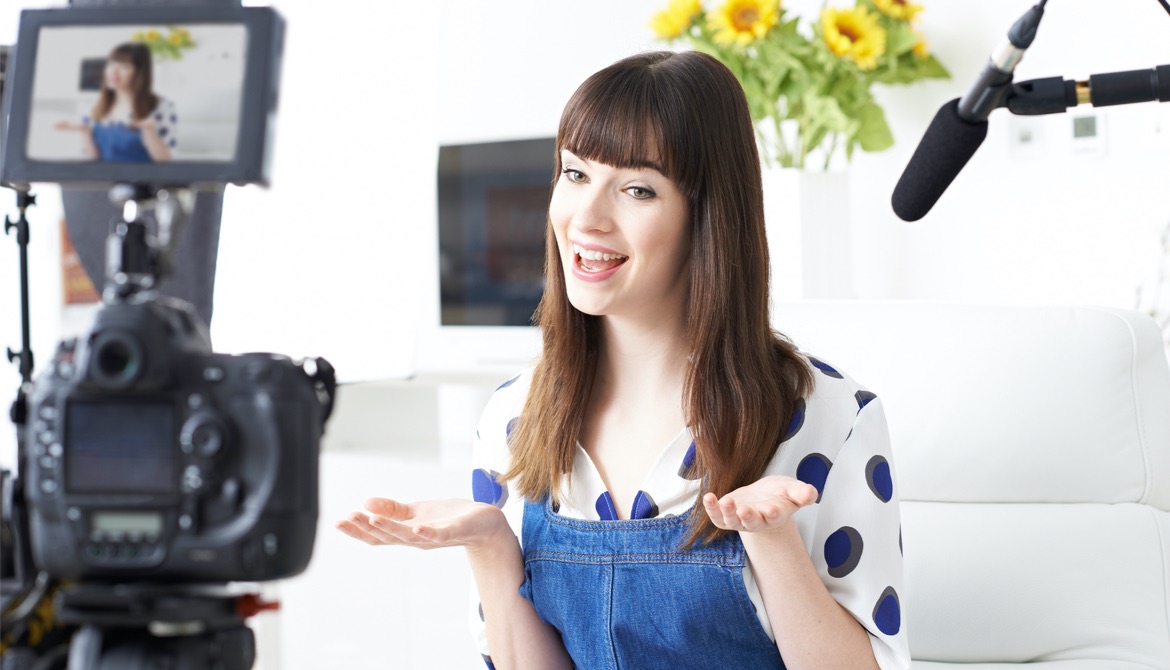 smiling young woman in polka dot shirt records video in front of camera and microphone