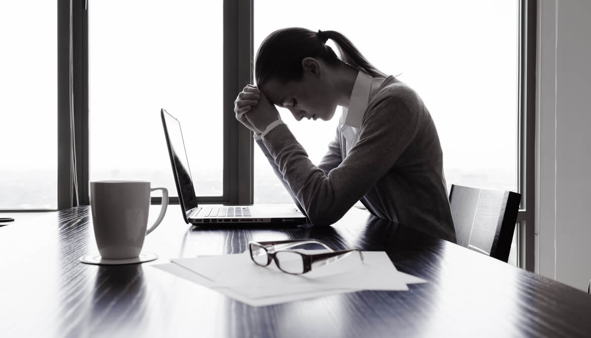 depressed female employee sitting alone at desk with head bowed