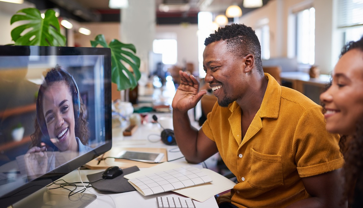 Smiling employees in office wave to coworker on screen during video conference call