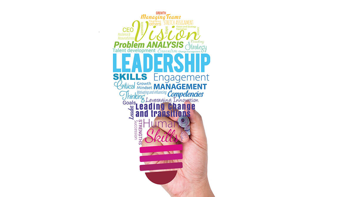 hand reaching out with a marker to write on a colorful word cloud of leadership-related terms shaped like a light bulb