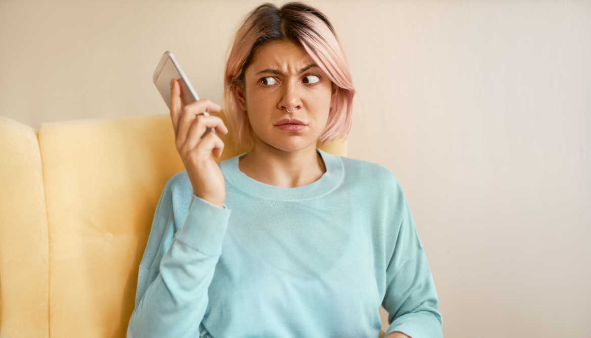 Portrait of frowning young woman in blue sweatshirt holding mobile phone