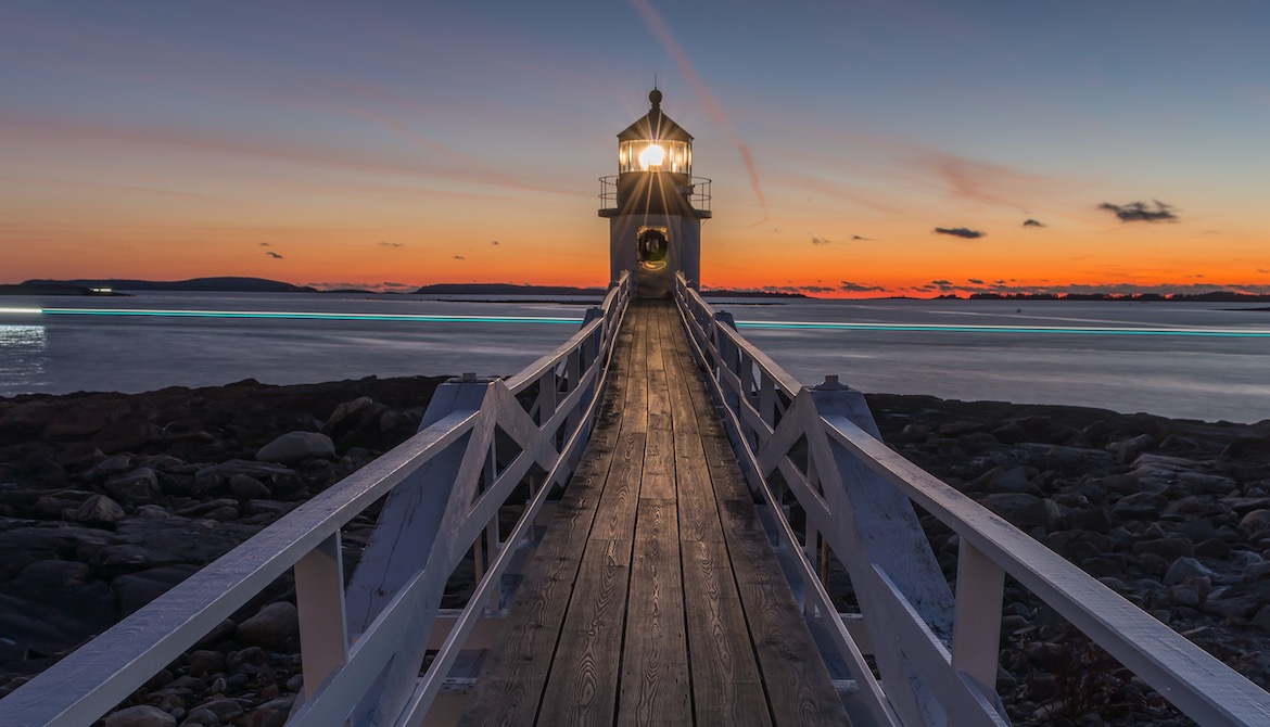 lighthouse shining in front of cloudy sunset sky