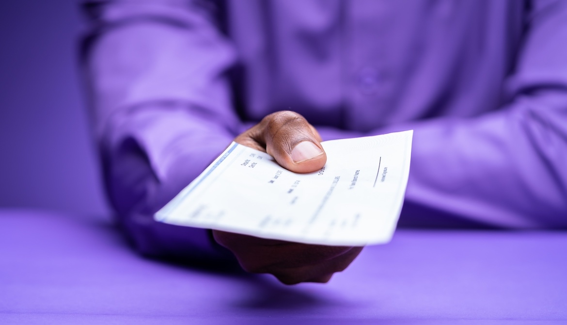 man in purple shirt holding out check for loan