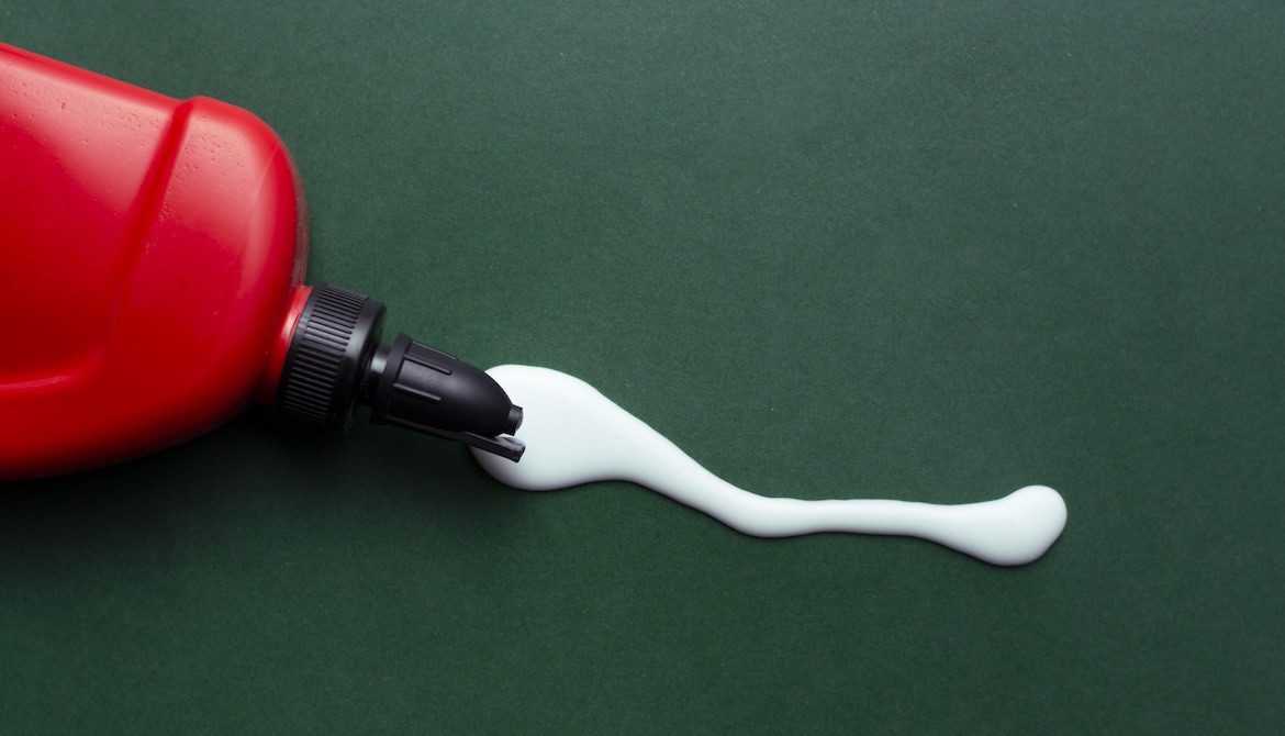 glue oozing out of a red bottle onto a green table