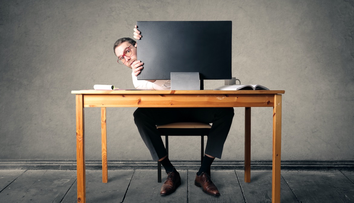 manager avoiding employees by hiding behind computer monitor at his desk