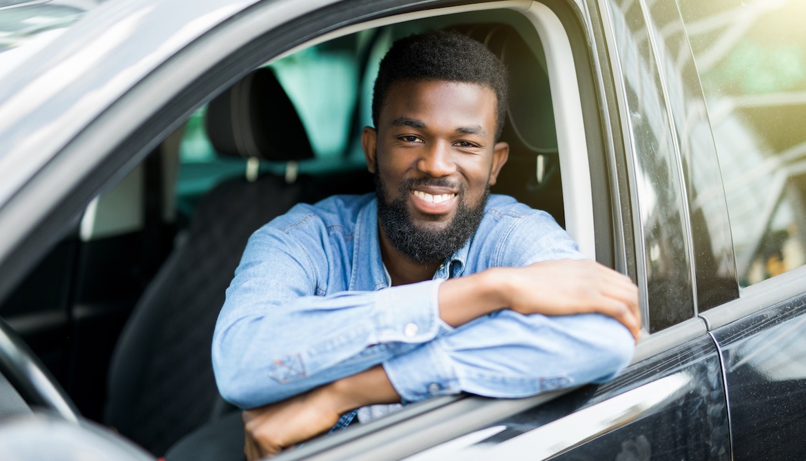 smiling young man sitting inside and leaning through open window of new car