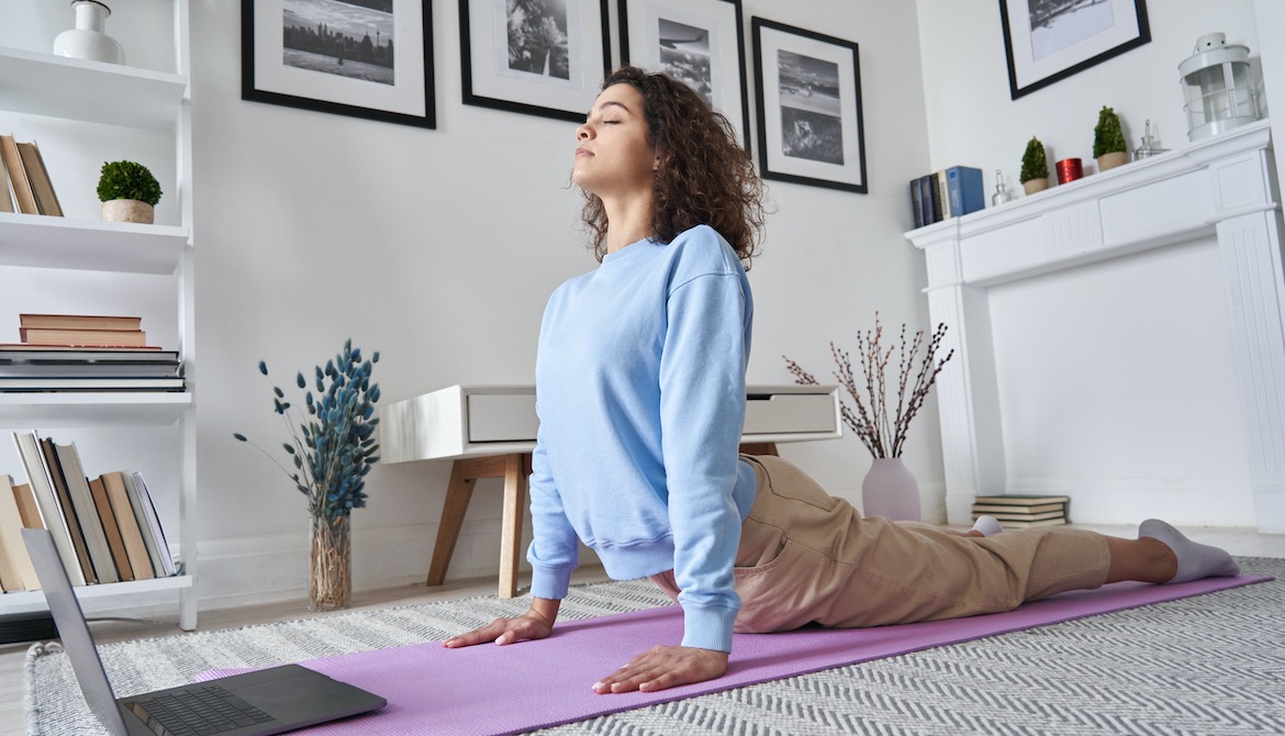 young woman doing yoga in home office while watching online video class