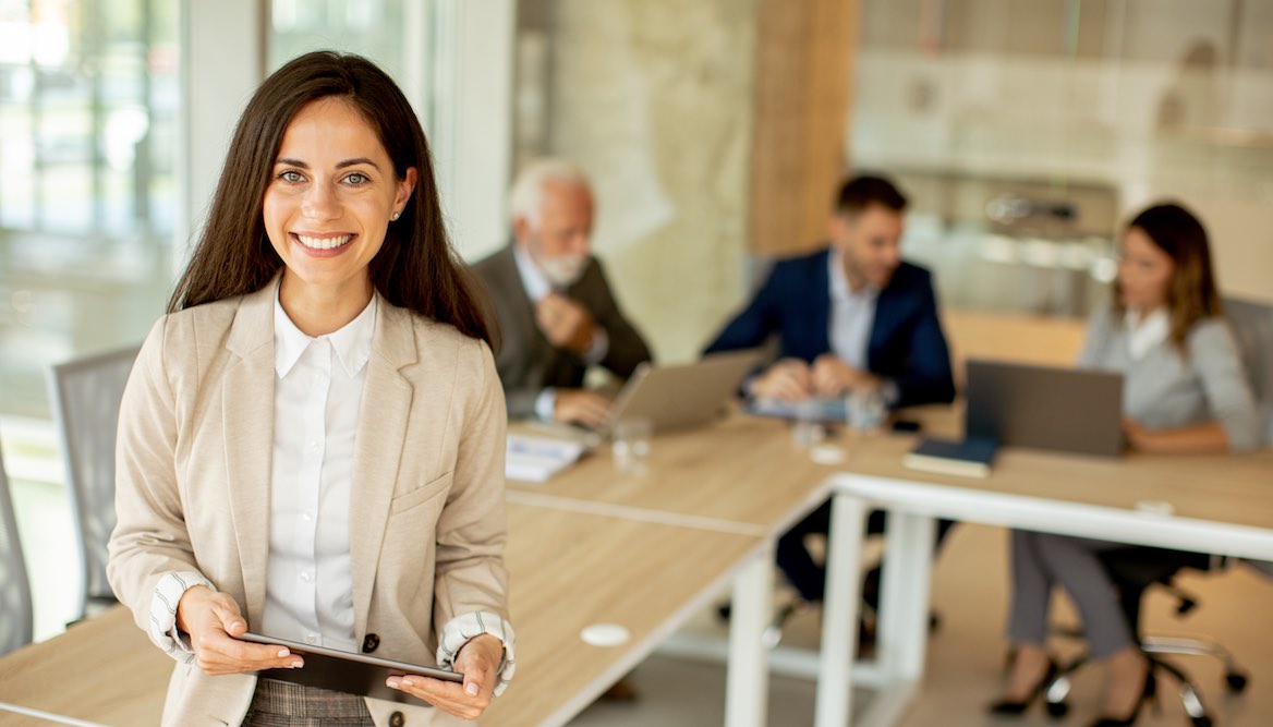 CEO sitting on table with tablet and team behind her