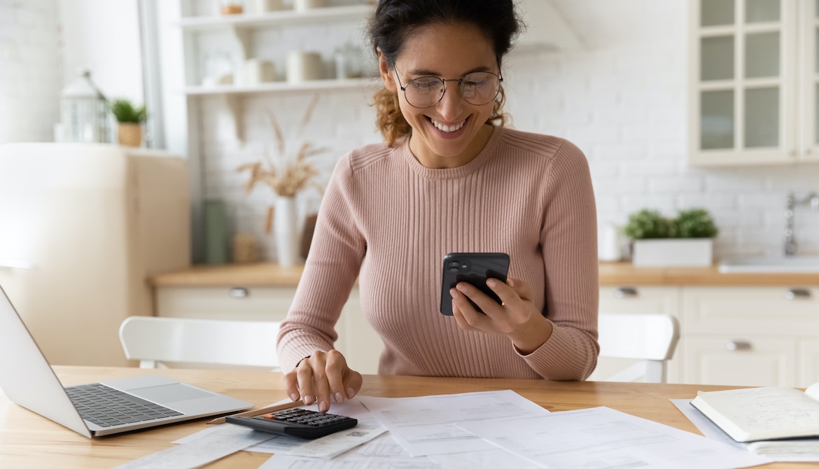 woman files at offer on smartphone while working on financial statements on calculator and laptop