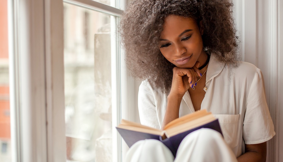 young African American businesswoman reading a book while sitting on window sill