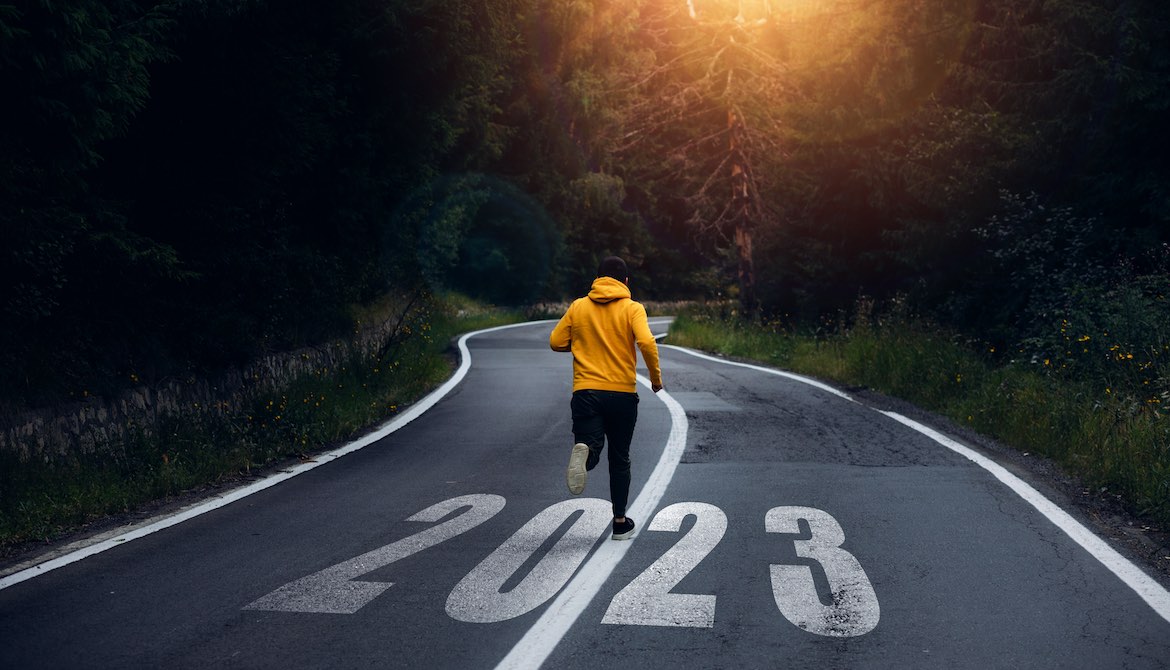 man in yellow hoodie jogging down road marked 2023 with bright sun peaking through the trees ahead