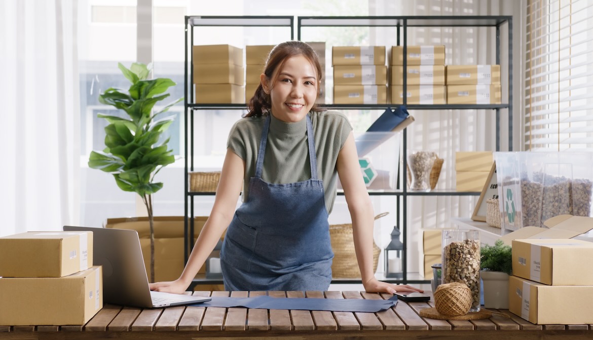 small business owner works on laptop while preparing packages for customers