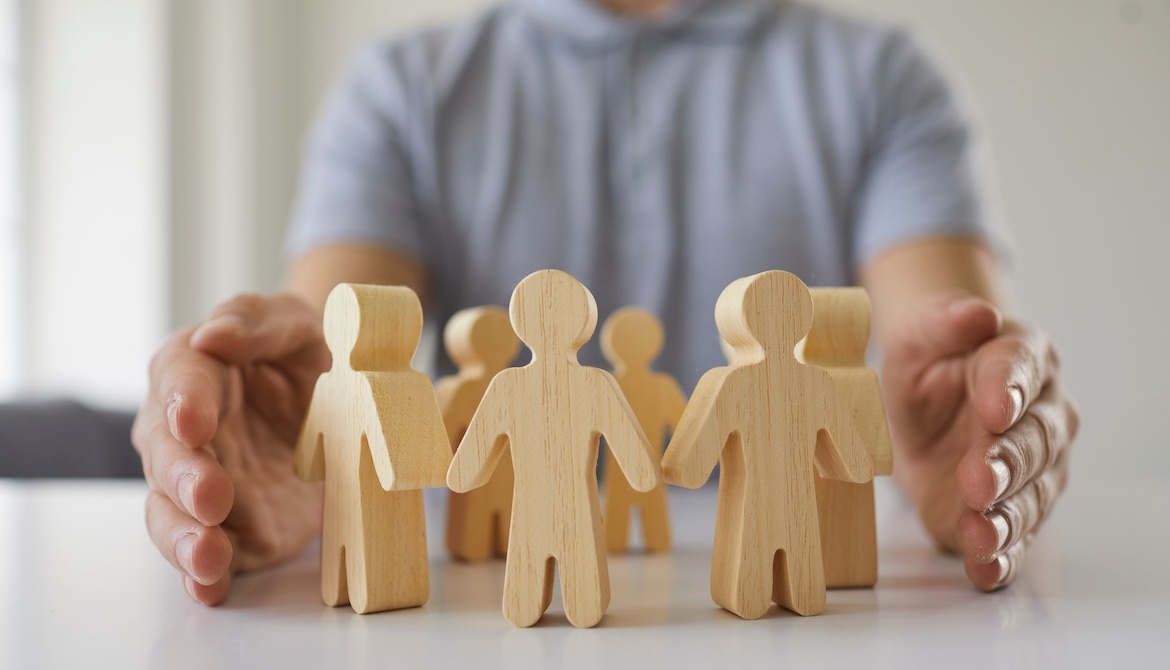 leader holds hands protectively around people figures representing workplace team