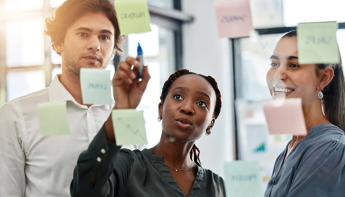 business leader points to board of sticky notes while working with employees