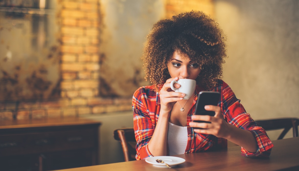 Gen Z woman drinking coffee and using smartphone for online banking at a cafe