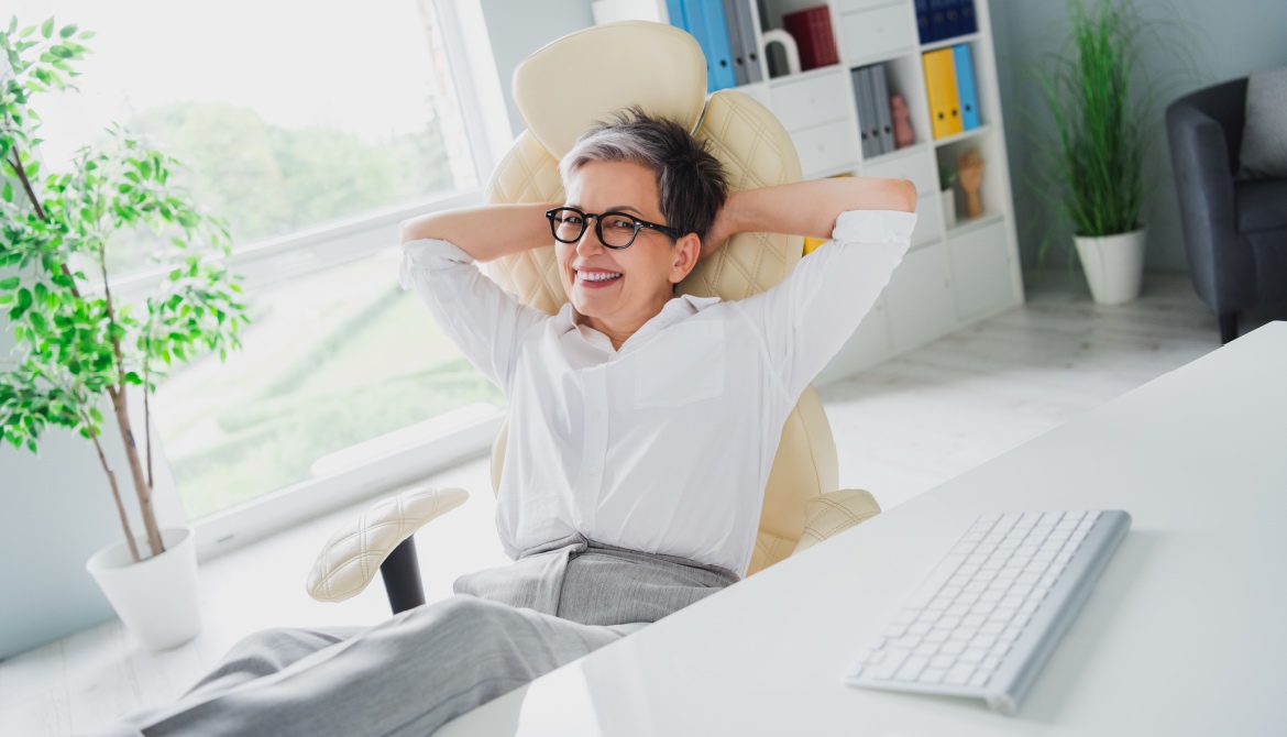 Photo of cheerful older businesswoman with her hands over her head at a desk isolated in an office