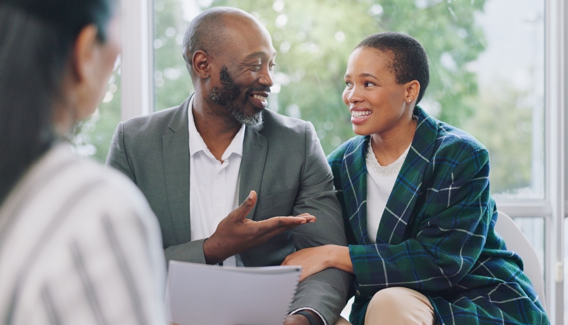 A smiling black couple sits across a desk from another person