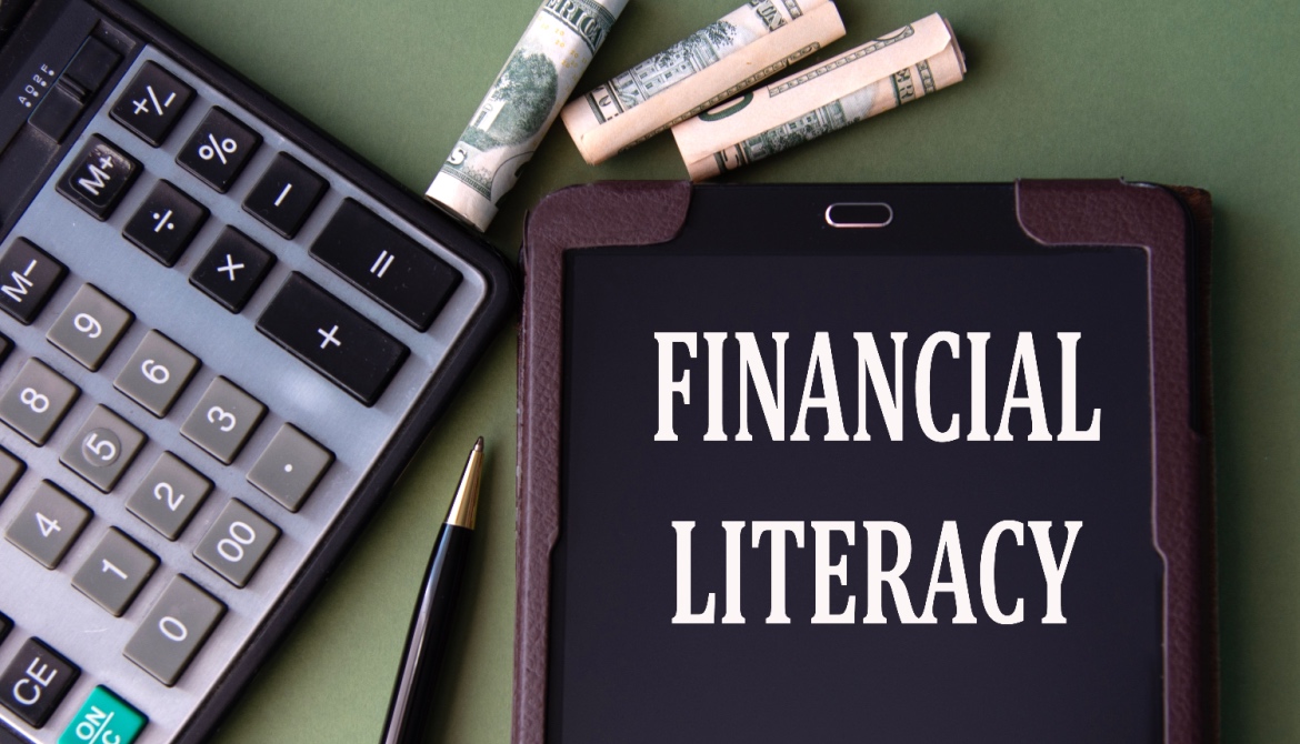 FINANCIAL LITERACY words appear on the screen of a tablet next to a calculator and banknotes