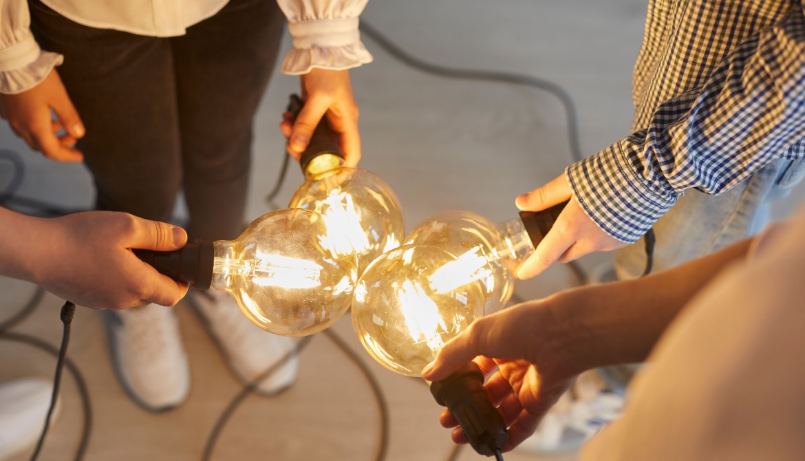 Close up of bright light bulb in the hands of different people