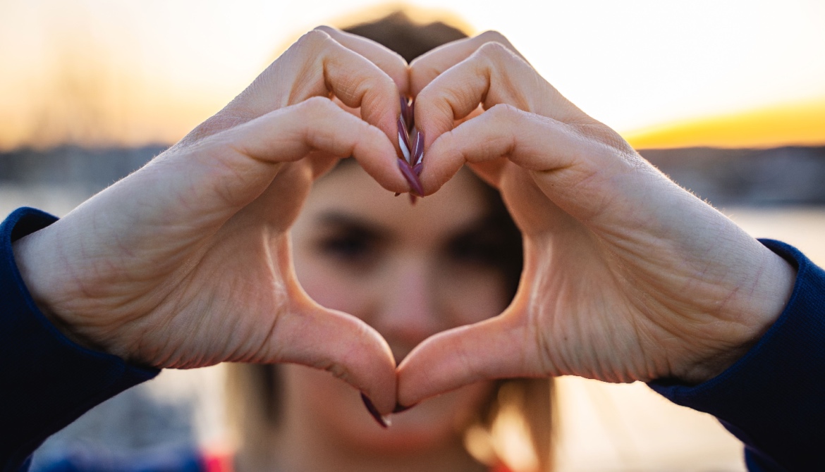 A young Gen Z woman creates a heart shape with her hands