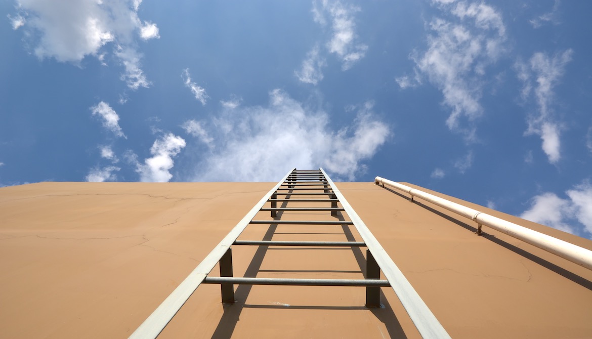 ladder leaning against biege stucco wall leading up to blue sky