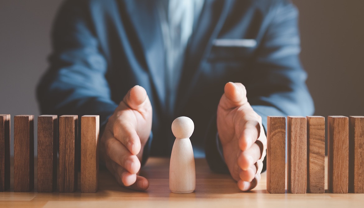 business leader protecting wooden person from falling dominoes