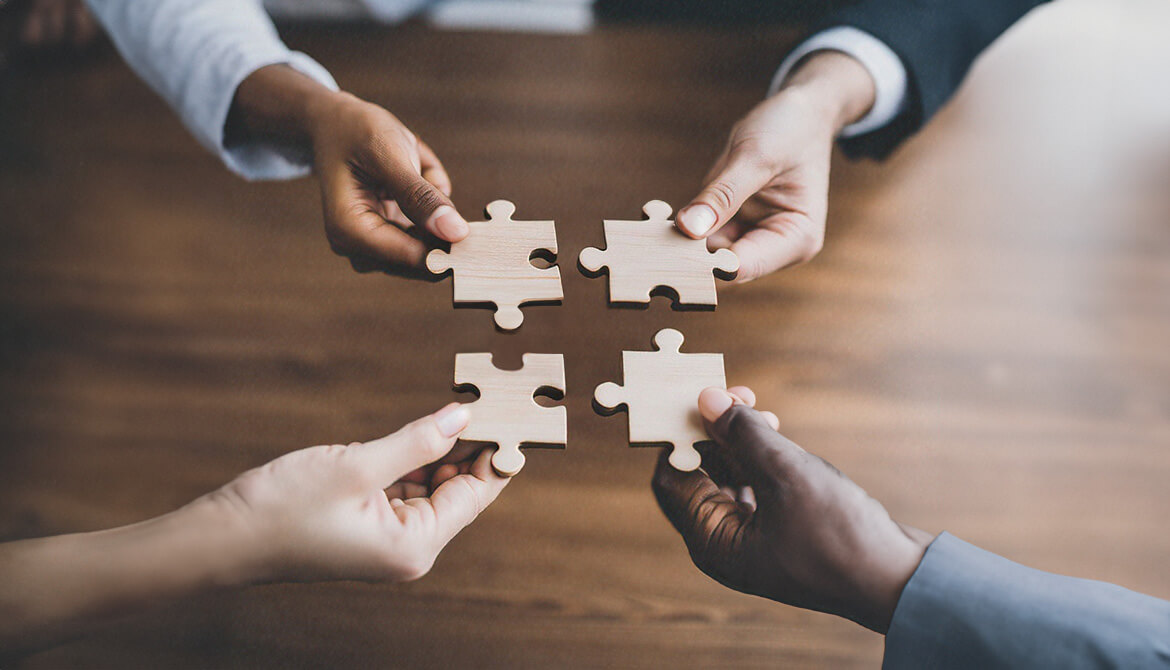 four hands holding puzzle pieces bringing them all together in the center