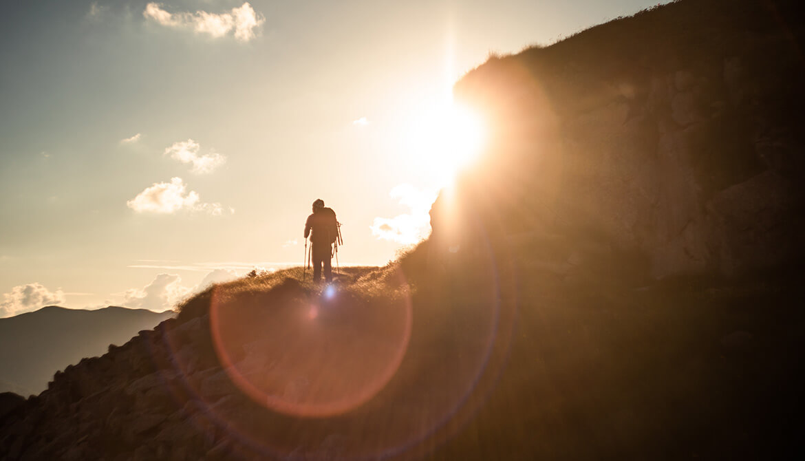 man climbing mountain walking into the sun