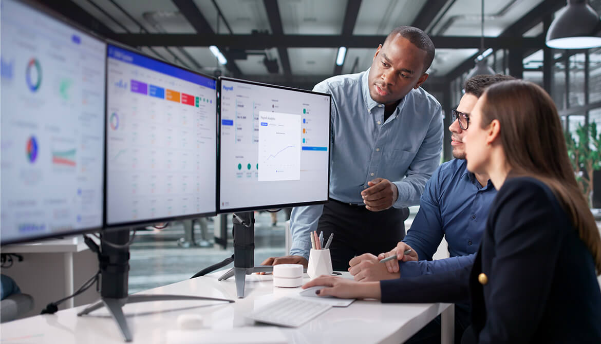 individuals looking at a 3 monitor set up while talking