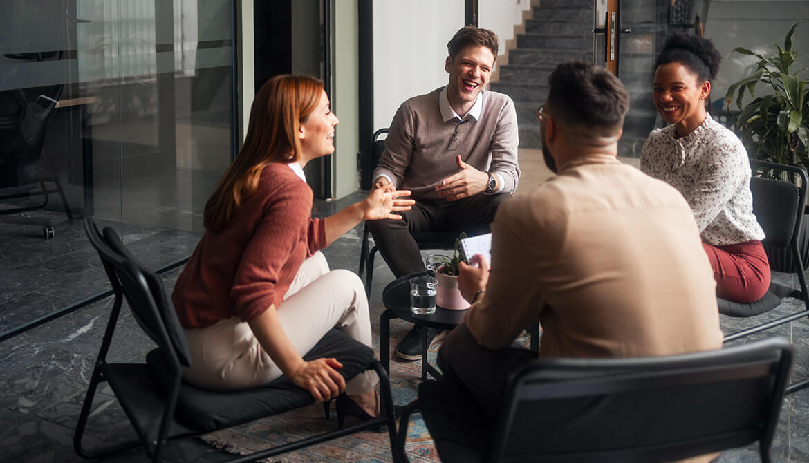 4 individuals sitting on a patio around a table laughing and talking
