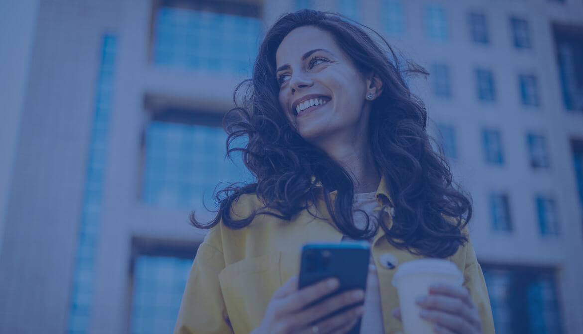 woman holding cell phone and coffee smiling over her shoulder