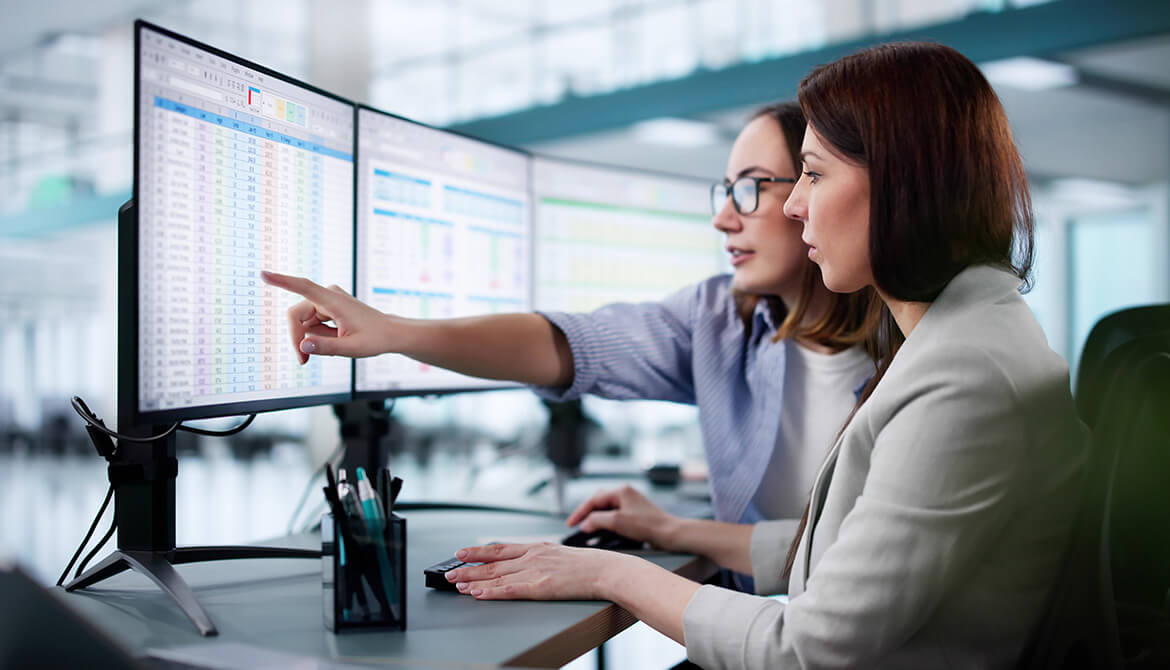 2 women looking at computer monitors filled with spreadsheets