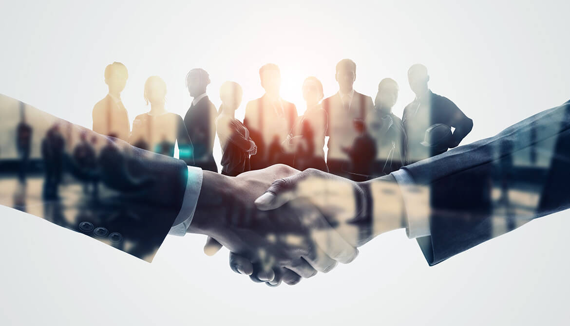 close up of a handshake with silhouette of individuals behind the joined hands