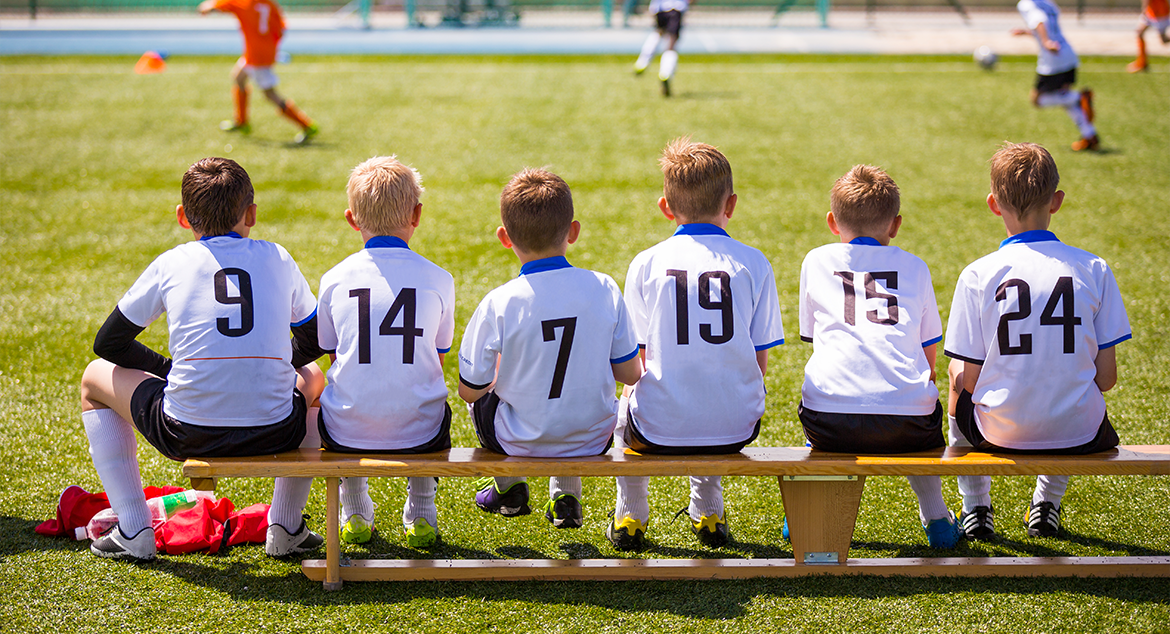 children's sports team sitting on the bench watching the game