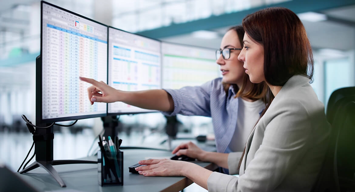 2 women looking at computer monitors filled with spreadsheets