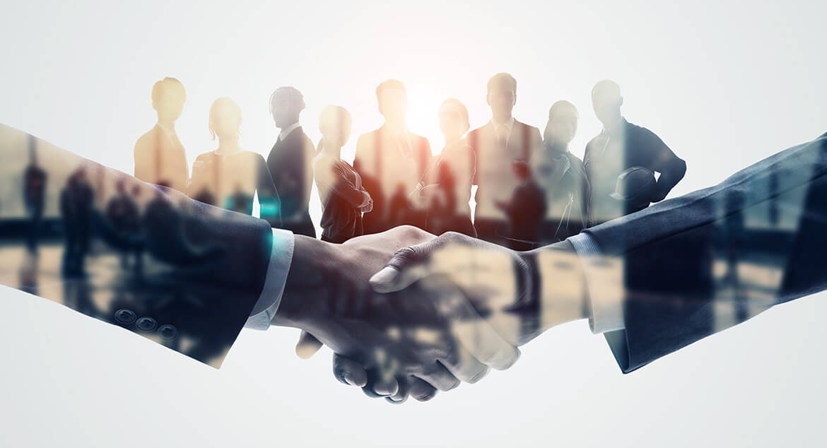 close up of a handshake with silhouette of individuals behind the joined hands