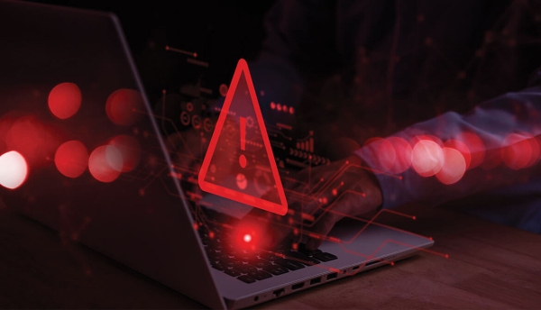 hands typing on laptop keyboard while large red warning triangle sign displays in front of screen