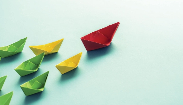 red paper boat leads a team of yellow boats leading a bigger team of green boats across the page