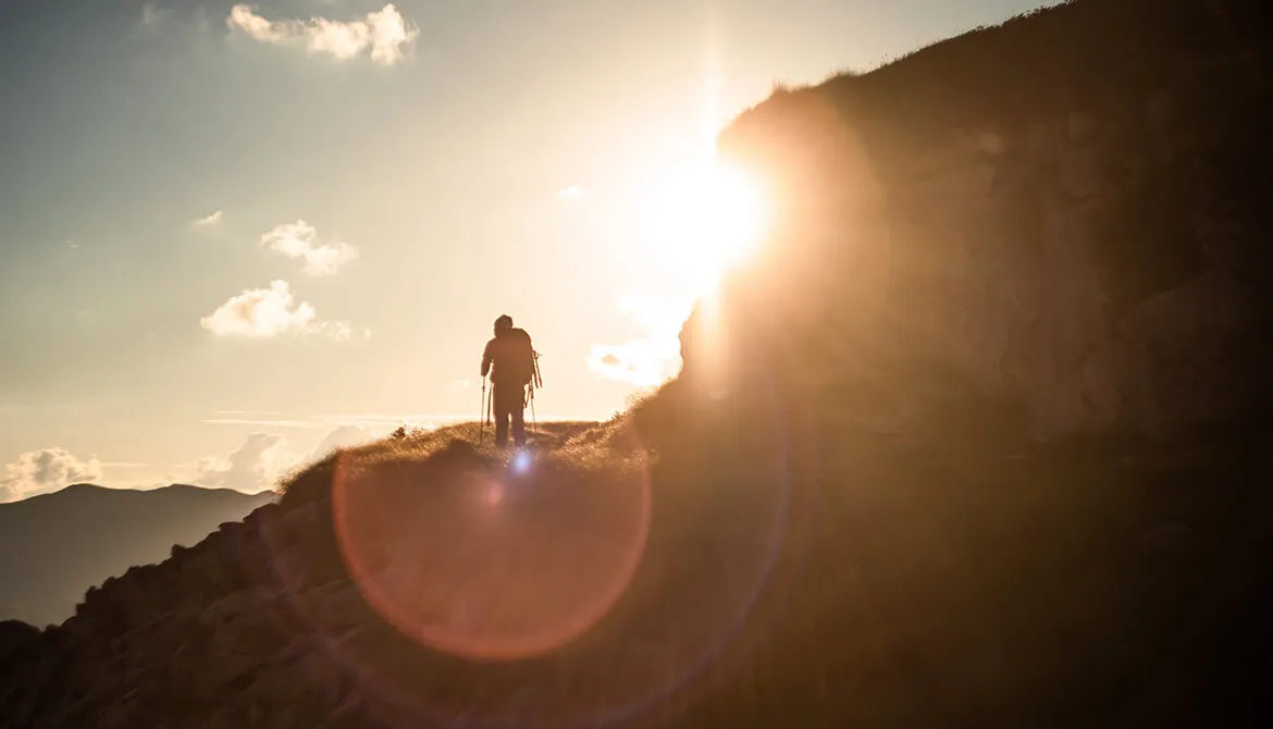 man climbing mountain walking into the sun